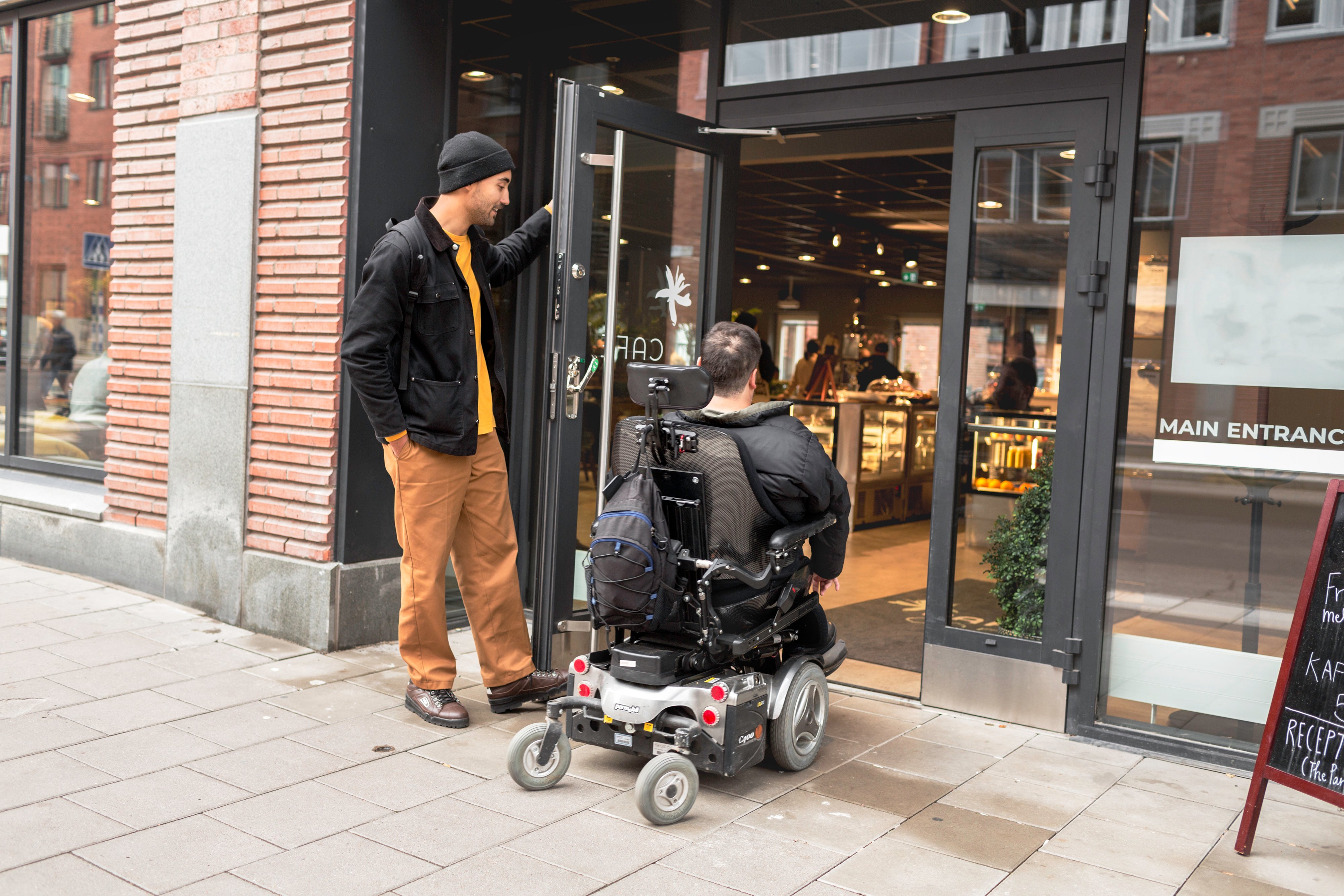 Personlig assistent öppnar dörren till en person som använder permobil