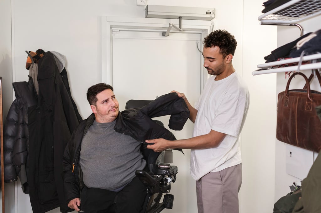 ST: En assistent assisterar assistansanvändaren att ta på sig jackan.