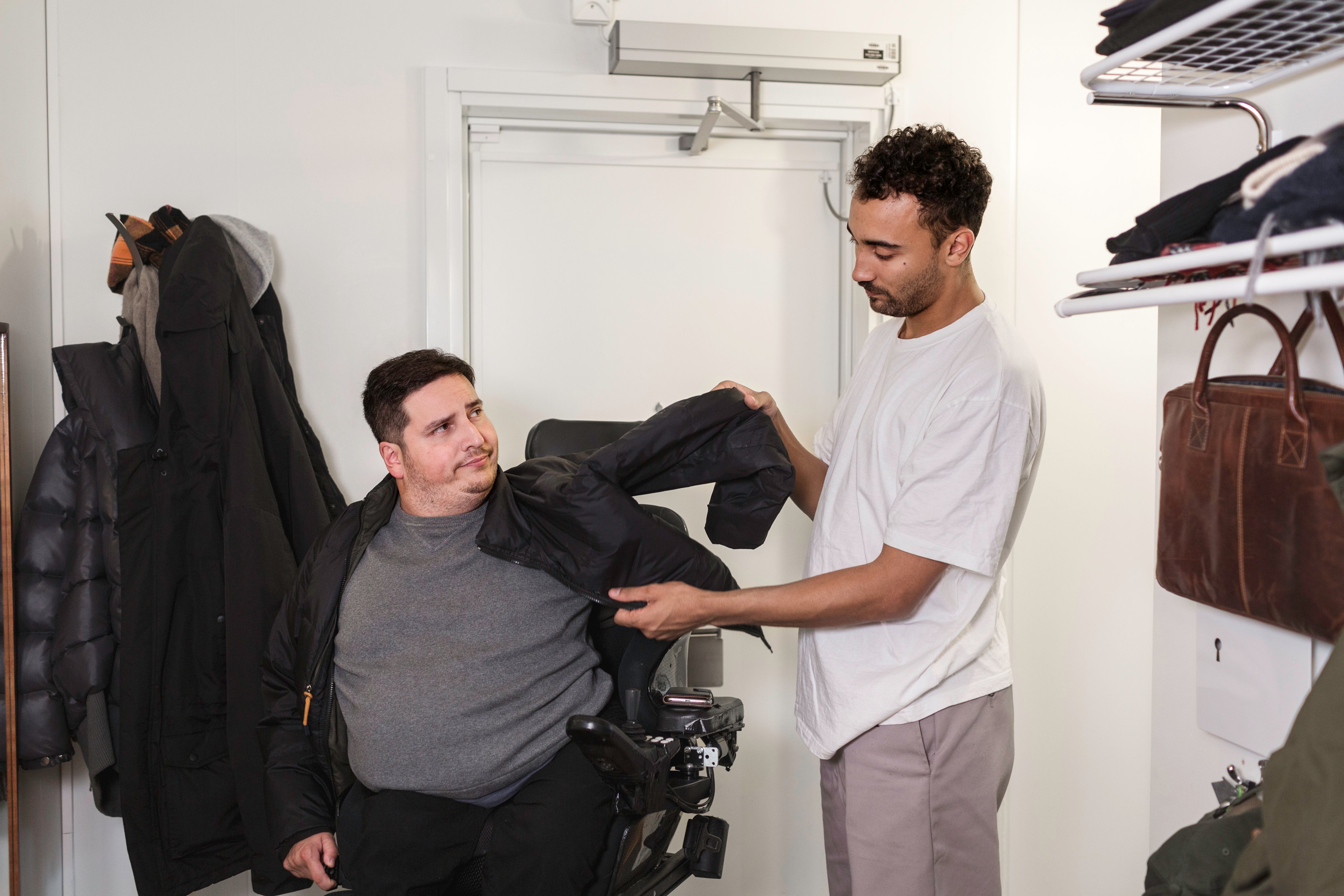 ST: En assistent assisterar assistansanvändaren att ta på sig jackan.