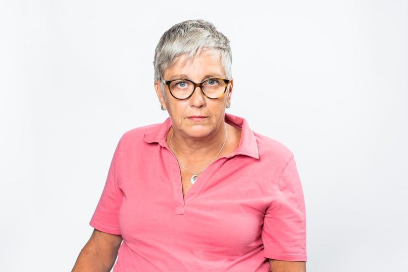 Suzanne Elmqvist_ Har en rosa tröja på sig, har kort grått hår,glasögon och en allvarlig blick
