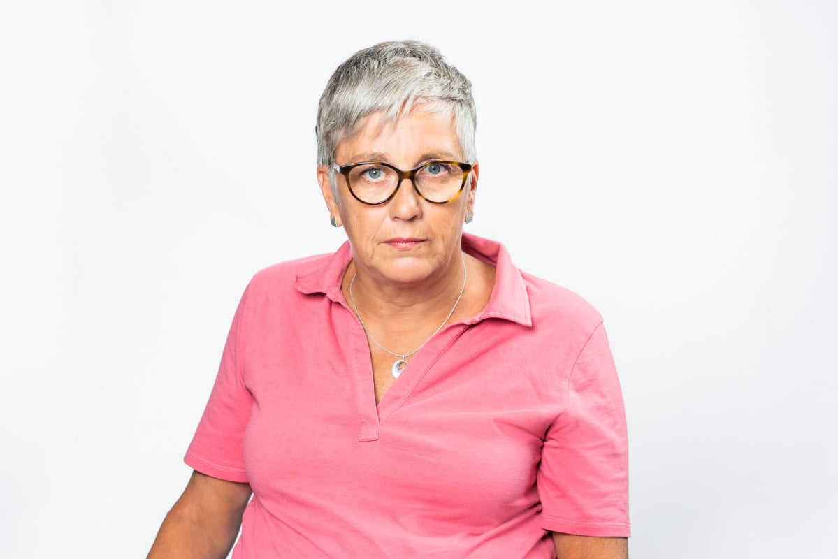 Suzanne Elmqvist_ Har en rosa tröja på sig, har kort grått hår,glasögon och en allvarlig blick