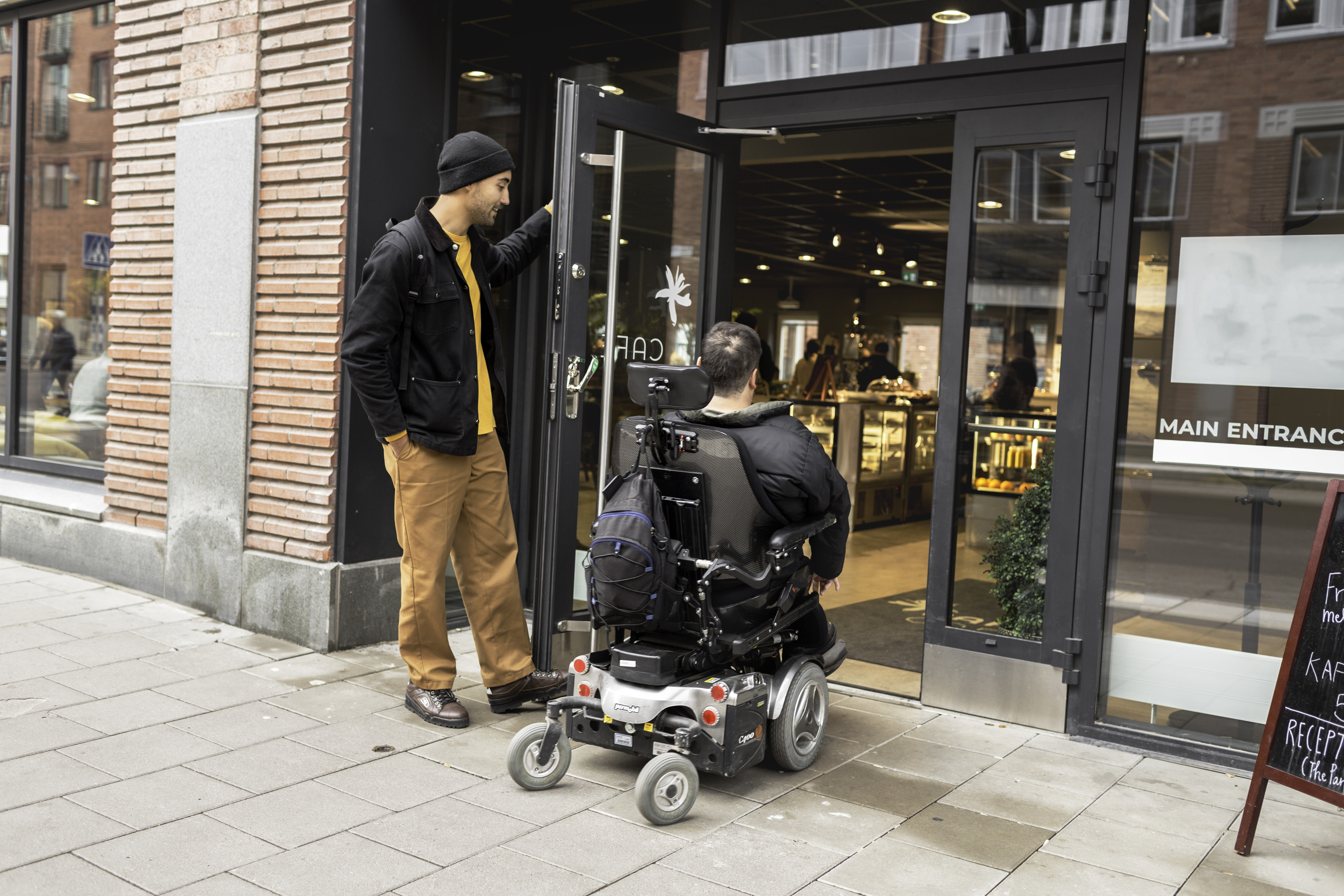 Personlig assistent öppnar dörren till en person som använder permobil