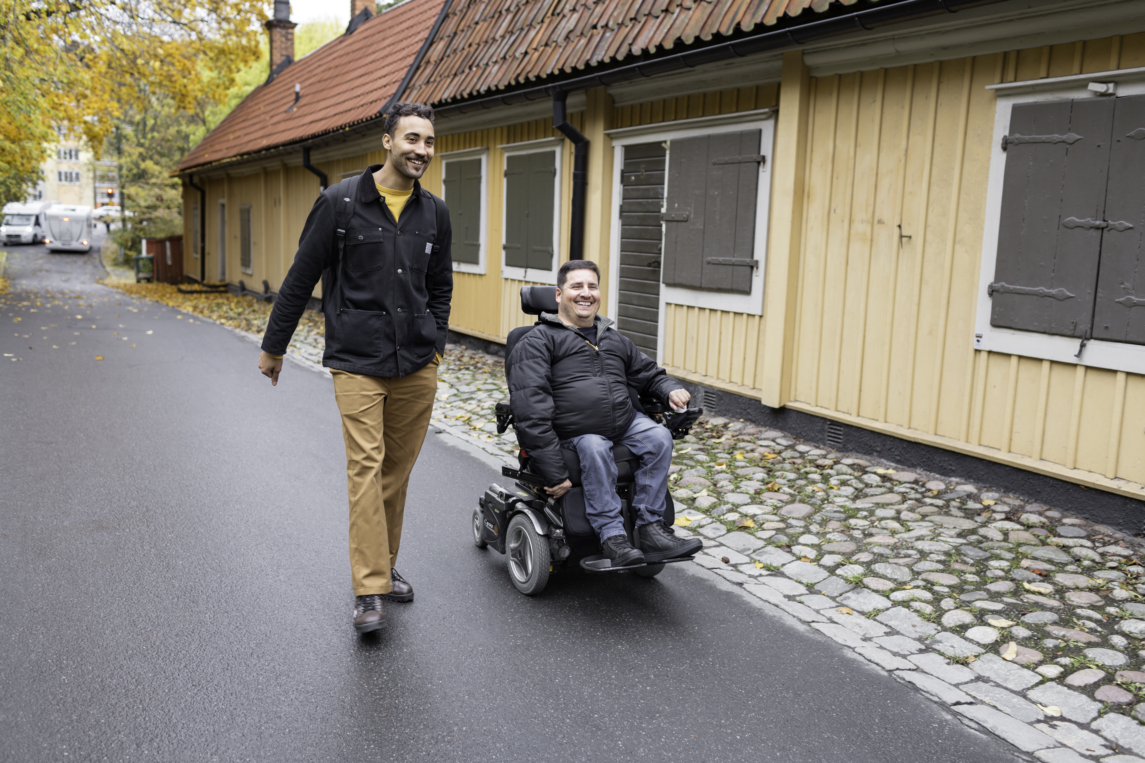 Bild på en assistansanvändare och en personlig assistent på promenad. Båda är glada. 